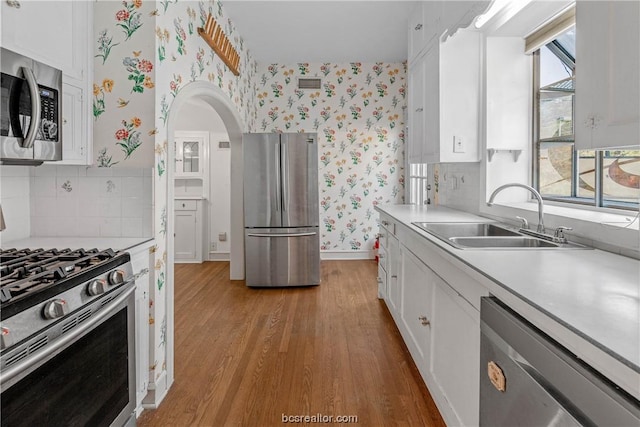 kitchen featuring backsplash, sink, light wood-type flooring, white cabinetry, and stainless steel appliances