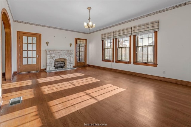 unfurnished living room with hardwood / wood-style flooring, a stone fireplace, ornamental molding, and an inviting chandelier