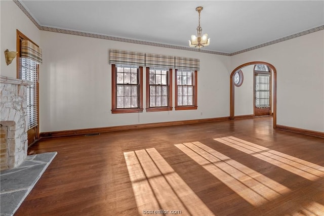 unfurnished living room with a healthy amount of sunlight, ornamental molding, dark wood-type flooring, and an inviting chandelier