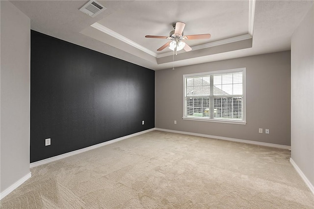 spare room featuring visible vents, baseboards, light colored carpet, a tray ceiling, and crown molding