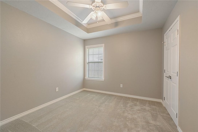 unfurnished room with baseboards, light colored carpet, ceiling fan, ornamental molding, and a tray ceiling