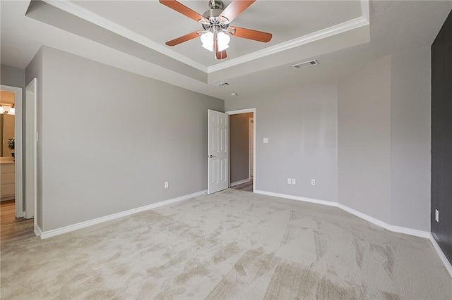 empty room featuring a tray ceiling, visible vents, crown molding, and baseboards