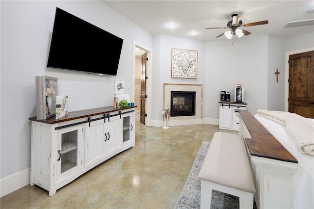 living area featuring finished concrete floors, a ceiling fan, baseboards, and a glass covered fireplace