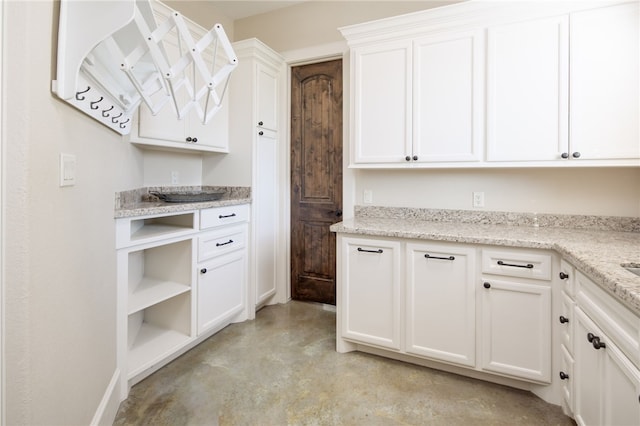 kitchen featuring finished concrete flooring, baseboards, light stone countertops, open shelves, and white cabinetry