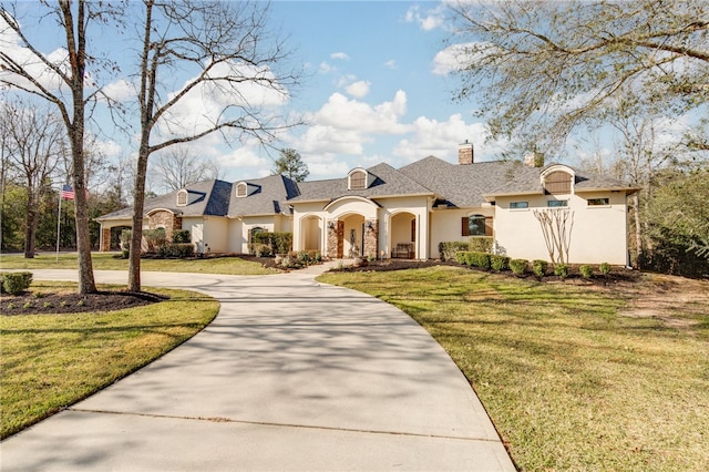 french country home with stucco siding, curved driveway, a chimney, and a front yard