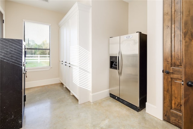 kitchen featuring finished concrete floors, stainless steel refrigerator with ice dispenser, and white cabinetry