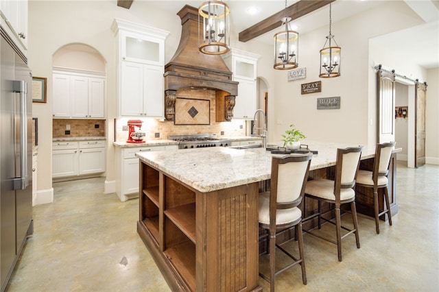 kitchen featuring tasteful backsplash, stainless steel built in fridge, a barn door, arched walkways, and a kitchen island with sink