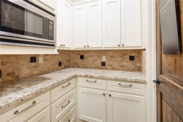 kitchen with stainless steel microwave, light stone countertops, tasteful backsplash, and white cabinets