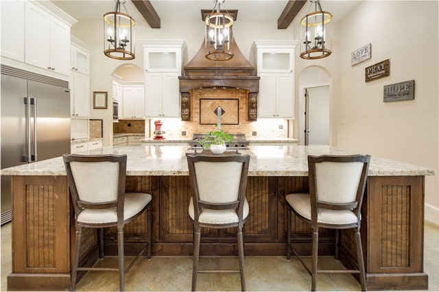 kitchen featuring a spacious island, arched walkways, stainless steel appliances, white cabinetry, and backsplash