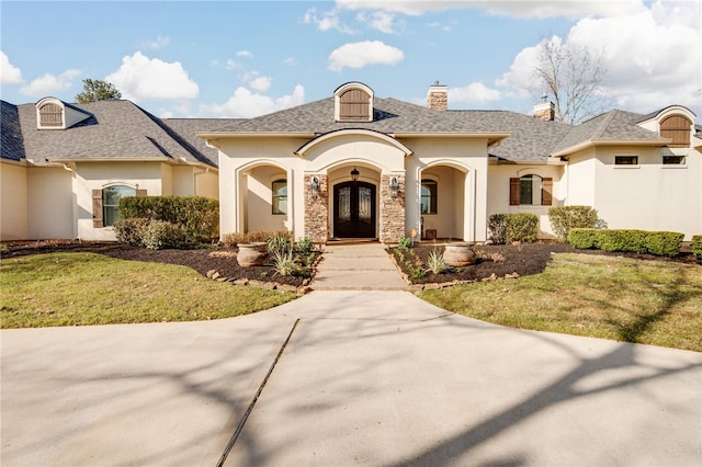 view of front of home featuring stucco siding, french doors, roof with shingles, a front yard, and a chimney