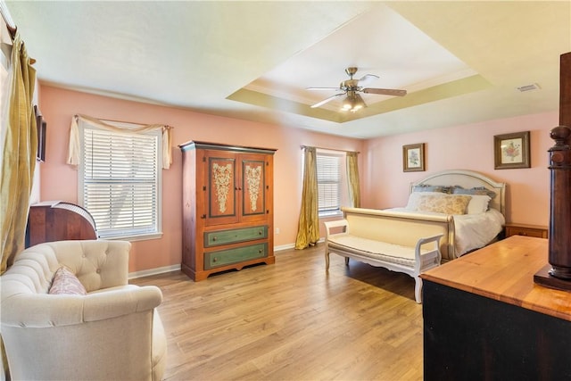 bedroom with light wood-type flooring, ornamental molding, ceiling fan, and a raised ceiling