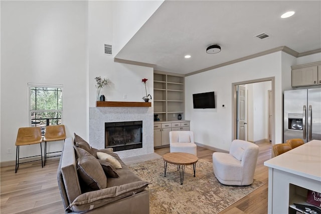 living room with visible vents, a fireplace with flush hearth, ornamental molding, and light wood-style flooring