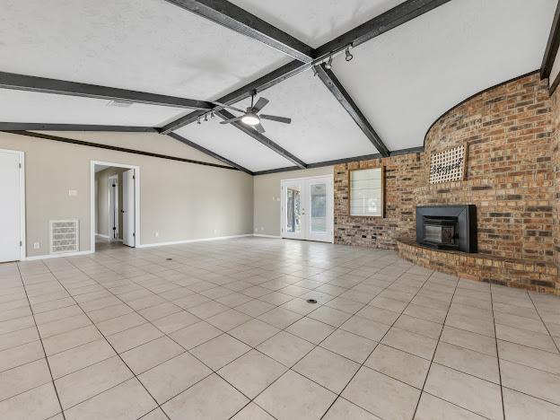 unfurnished living room with vaulted ceiling with beams, ceiling fan, light tile patterned floors, and brick wall