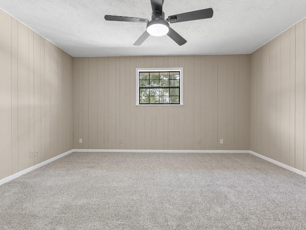 carpeted spare room with ceiling fan, wood walls, and a textured ceiling