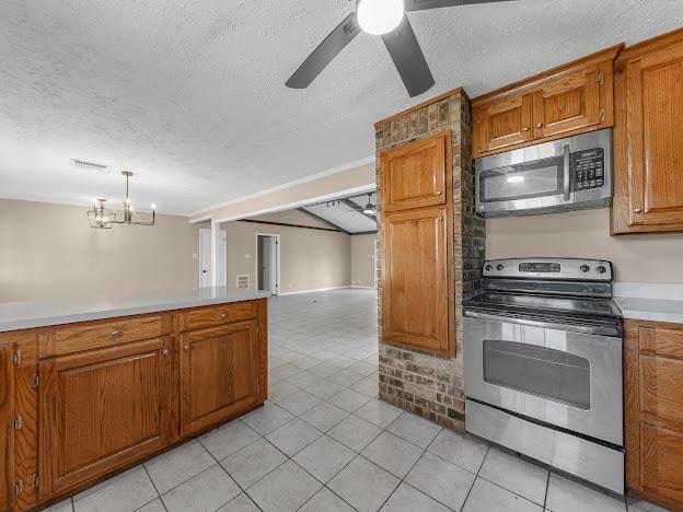 kitchen with a textured ceiling, light tile patterned floors, stainless steel appliances, and hanging light fixtures