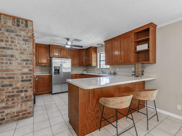 kitchen featuring ceiling fan, stainless steel fridge with ice dispenser, kitchen peninsula, a kitchen bar, and light tile patterned floors