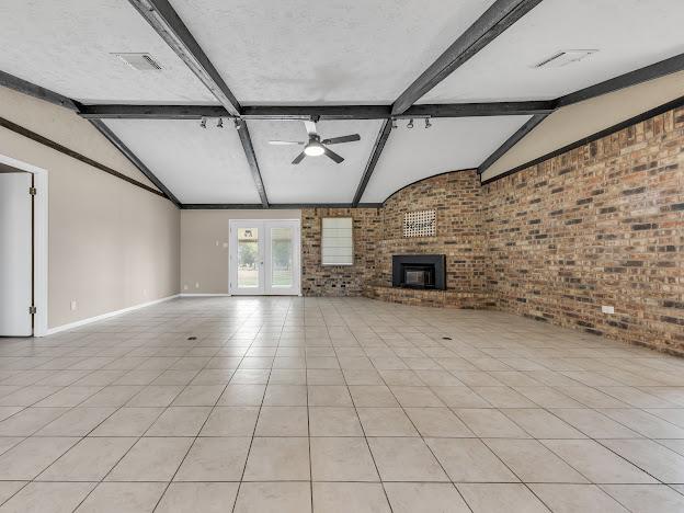 unfurnished living room featuring lofted ceiling with beams, ceiling fan, light tile patterned flooring, and brick wall