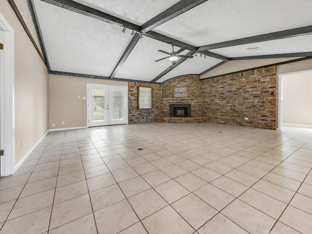 unfurnished living room with ceiling fan, light tile patterned floors, brick wall, and french doors