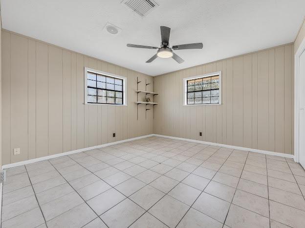 tiled empty room with ceiling fan and wooden walls