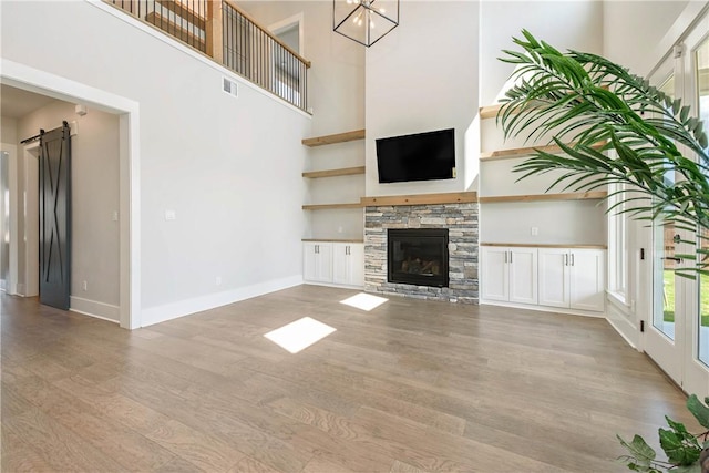 unfurnished living room with a barn door, light wood-type flooring, a fireplace, and a high ceiling