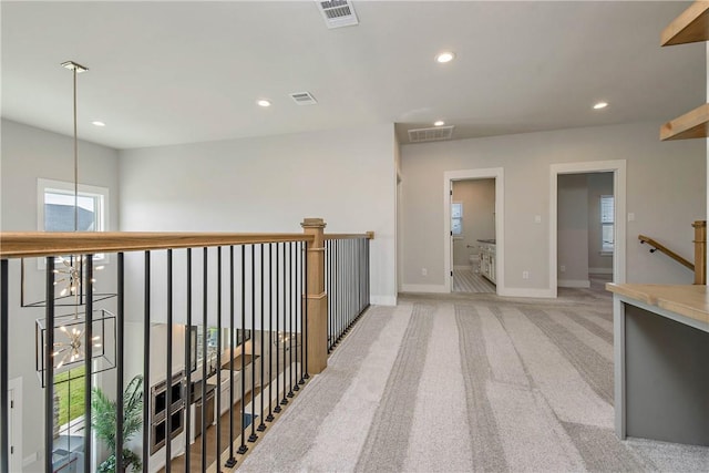 hallway with light carpet and a notable chandelier