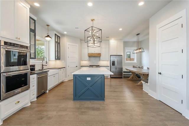 kitchen featuring a kitchen island, stainless steel appliances, hanging light fixtures, and light hardwood / wood-style flooring