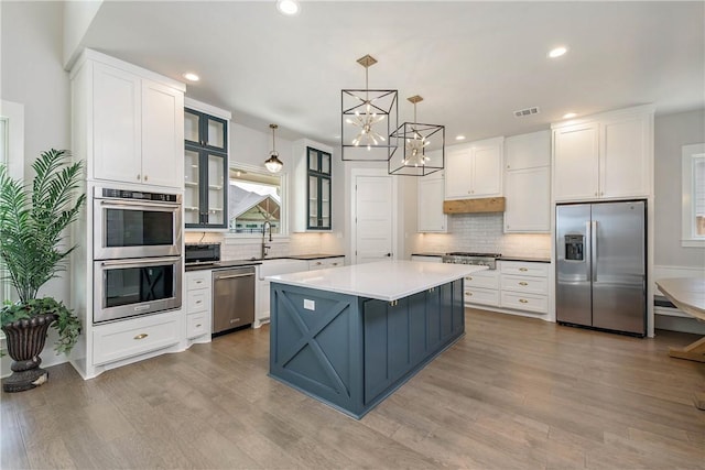 kitchen featuring pendant lighting, a center island, appliances with stainless steel finishes, light hardwood / wood-style floors, and white cabinetry