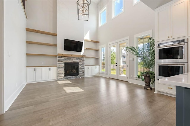 unfurnished living room with hardwood / wood-style flooring, a stone fireplace, a towering ceiling, and an inviting chandelier