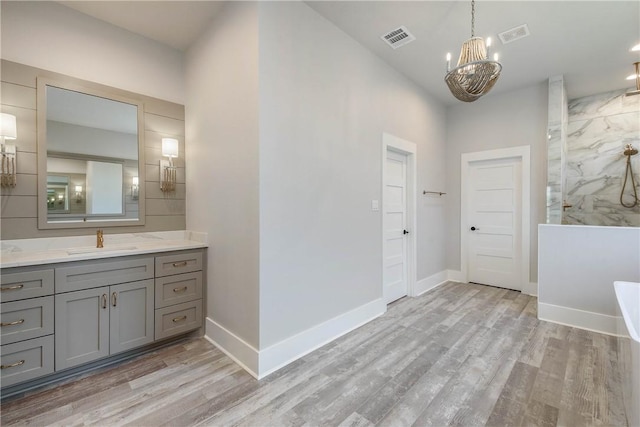 bathroom with hardwood / wood-style flooring, vanity, a tile shower, and an inviting chandelier