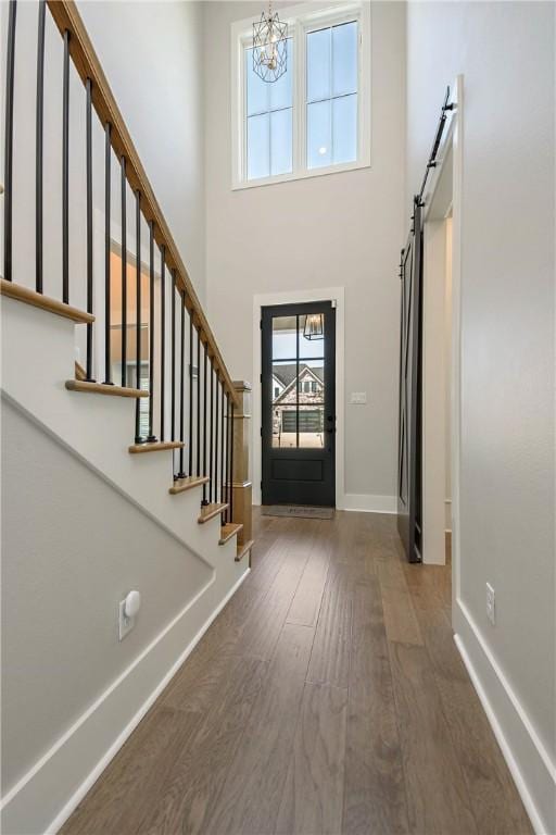 foyer entrance with a towering ceiling, a barn door, dark wood-type flooring, and a notable chandelier