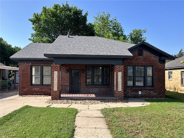 view of front facade featuring brick siding, a porch, a front lawn, and a shingled roof