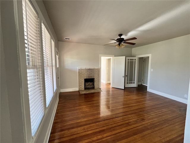 unfurnished living room with ceiling fan, baseboards, a brick fireplace, and dark wood-style floors