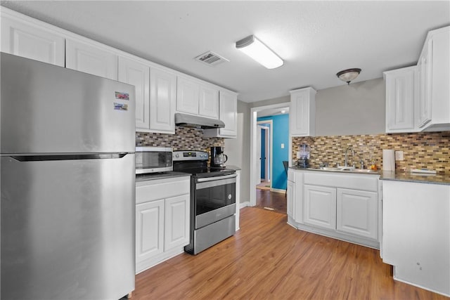 kitchen with stainless steel appliances, white cabinetry, and light hardwood / wood-style flooring