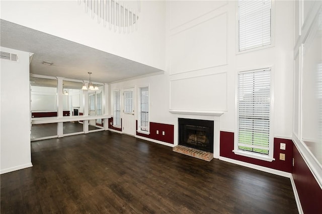 unfurnished living room with dark hardwood / wood-style flooring, a towering ceiling, a textured ceiling, and an inviting chandelier