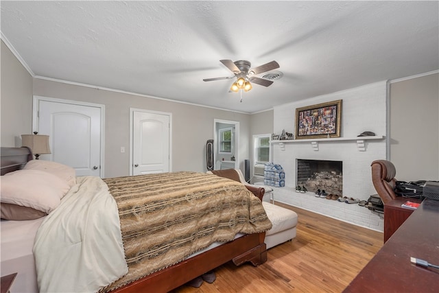 bedroom with crown molding, a brick fireplace, a ceiling fan, and wood finished floors