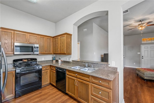 kitchen with ceiling fan, sink, black appliances, stone countertops, and hardwood / wood-style flooring