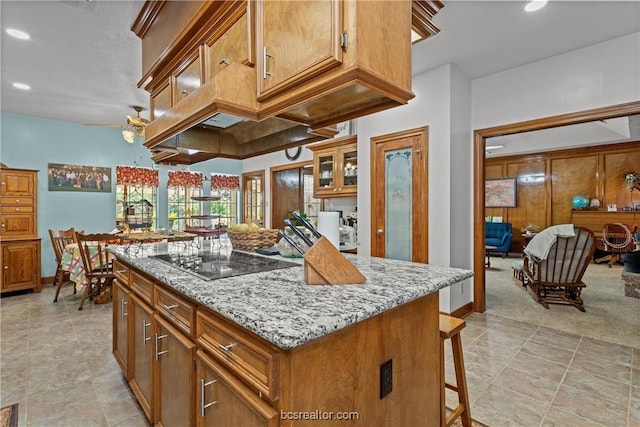 kitchen featuring light carpet, light stone counters, black electric cooktop, ceiling fan, and a kitchen island