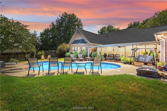 pool at dusk featuring a lawn, a patio, and an outdoor living space with a fire pit