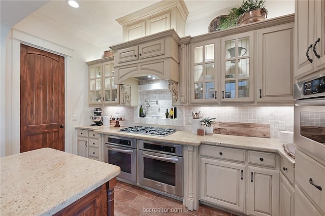 1650 Bird Pond Rd, College Station, TX 77845 - kitchen featuring stainless steel appliances, backsplash, ornamental molding, glass insert cabinets, and light stone counters