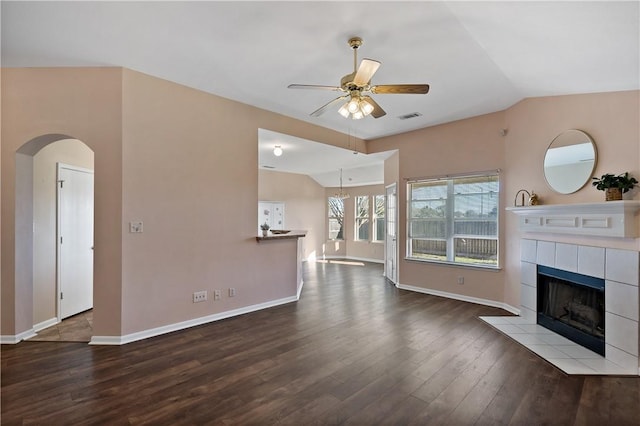 unfurnished living room with visible vents, wood finished floors, a fireplace, ceiling fan, and vaulted ceiling