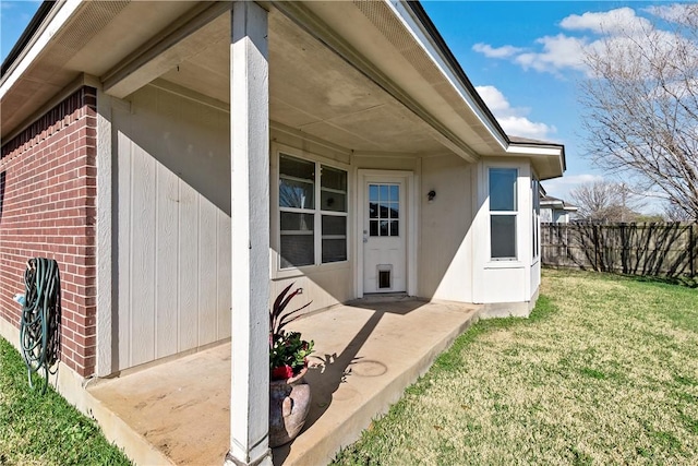 doorway to property with fence, brick siding, and a lawn