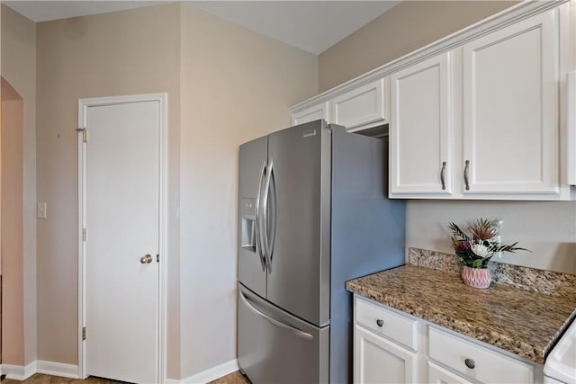 kitchen with stainless steel refrigerator with ice dispenser, arched walkways, white cabinets, stone counters, and baseboards