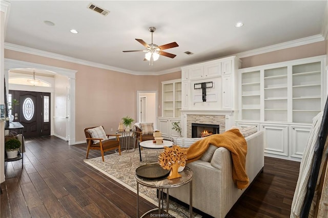 living room featuring a stone fireplace, built in features, dark hardwood / wood-style floors, and ornamental molding