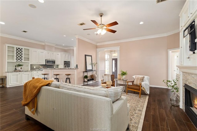 living room with ceiling fan, ornamental molding, a fireplace, and dark wood-type flooring