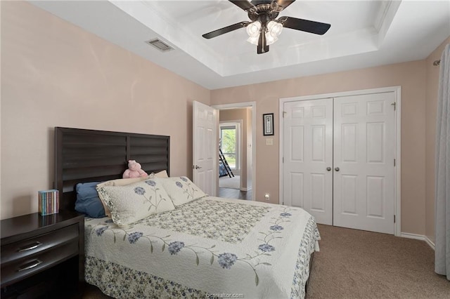 carpeted bedroom featuring a tray ceiling, ceiling fan, and a closet