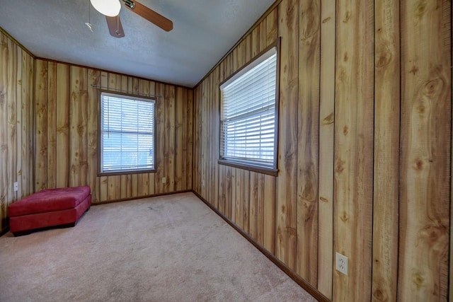 unfurnished room featuring ceiling fan, crown molding, light carpet, and wood walls