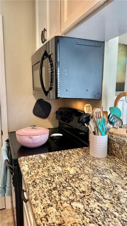 interior details with white cabinetry, light stone counters, black microwave, and electric range oven