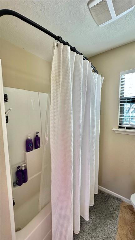 bathroom featuring a textured ceiling, shower / tub combo, and baseboards