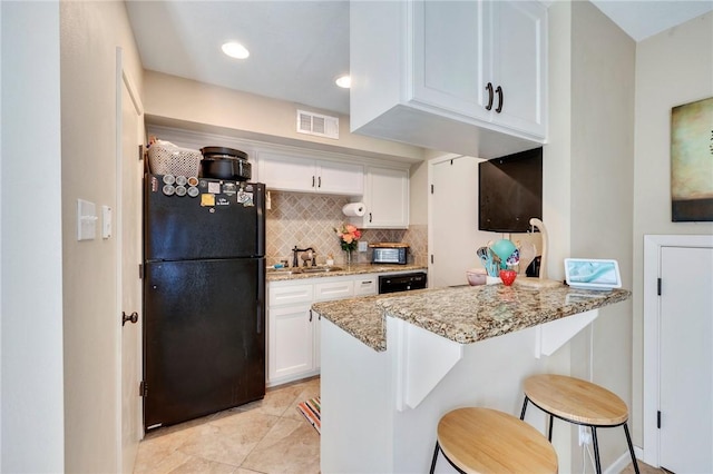 kitchen with visible vents, a sink, backsplash, freestanding refrigerator, and white cabinets