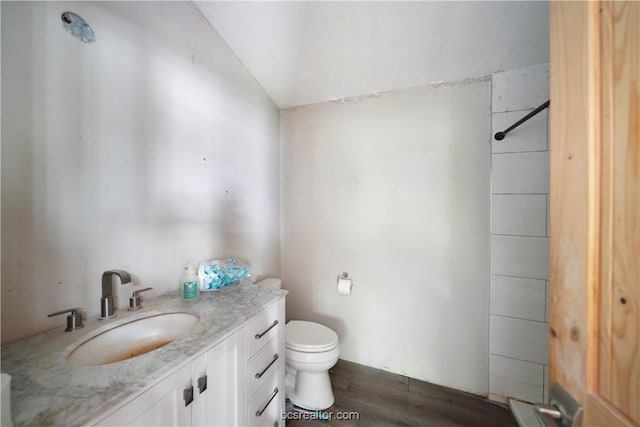 bathroom featuring wood-type flooring, vanity, toilet, and vaulted ceiling